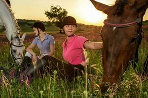 simpático mujer son sentado siguiente a un marrón y blanco caballos, cuales pastado en el prado. foto