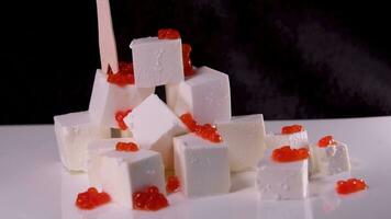 Close up view of soft feta cheese cube placed into white bowl with the kitchen knife with caviar video