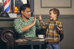 Young father and his stylish little son in the barbershop in the waiting room. photo