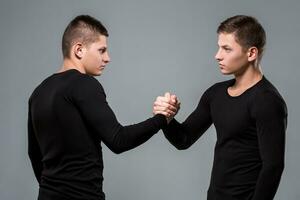 Portrait of young twin brothers standing face to face on gray ba photo