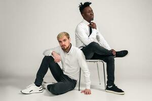 Joyful relaxed african and caucasian boys in white and black office clothes laughing and posing at white studio background with copy space photo