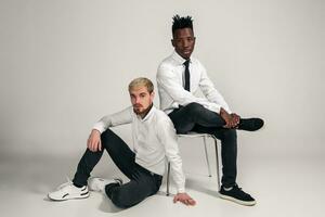 Joyful relaxed african and caucasian boys in white and black office clothes laughing and posing at white studio background with copy space photo