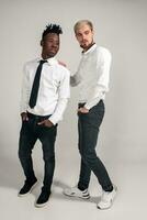 Joyful relaxed african and caucasian boys in white and black office clothes laughing and posing at white studio background with copy space photo