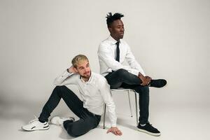 Joyful relaxed african and caucasian boys in white and black office clothes laughing and posing at white studio background with copy space photo