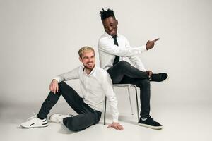 Joyful relaxed african and caucasian boys in white and black office clothes laughing and posing at white studio background with copy space photo