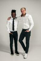 Joyful relaxed african and caucasian boys in white and black office clothes laughing and posing at white studio background with copy space photo