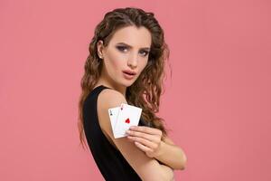 Young woman holding two aces in hand against on pink background photo