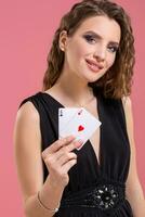 Young woman holding two aces in hand against on pink background photo