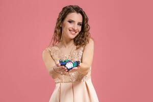 Young beautiful emotional woman with chips in hands on a pink background in the studio. Poker photo