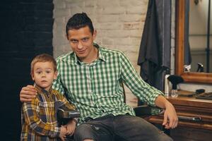 Young handsome father and his little stylish son at barbershop waiting for barber photo