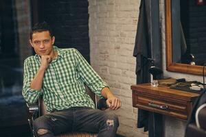 Handsome young man looking at the camera and sitting in a chair on at the barbershop photo