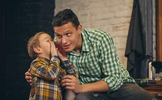 Young handsome father and his little stylish son at barbershop waiting for barber photo