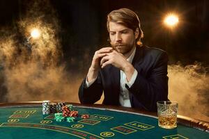 A man in a business suit sitting at the game table. Male player. Passion, cards, chips, alcohol, dice, gambling, casino - it is as male entertainment. photo