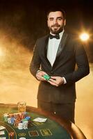 A young man in a business suit standing near poker table. Man gambles. photo