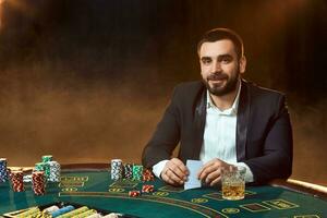 A young man in a business suit sitting at the poker table. Man gambles. The player at the gaming table playing cards. photo