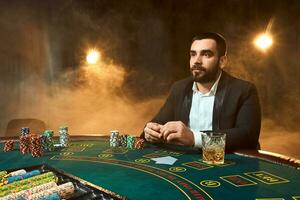 A young man in a business suit sitting at the poker table. Man gambles. The player at the gaming table playing cards. photo