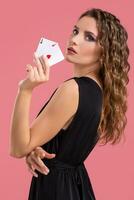 Young woman holding two aces in hand against on pink background photo