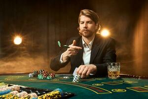 A man in a business suit sitting at the game table. Male player. Passion, cards, chips, alcohol, dice, gambling, casino - it is as male entertainment. photo