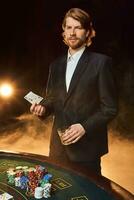 A man in a business suit standing near the game table. Male player. Passion, cards, chips, alcohol, dice, gambling, casino - it is as male entertainment. photo