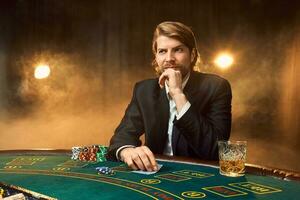 A man in a business suit sitting at the game table. Male player. Passion, cards, chips, alcohol, dice, gambling, casino - it is as male entertainment. photo