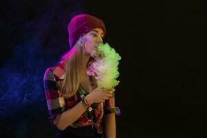 Vaping girl. Young hipster woman vape e-cig on black background. Hip-hop style. Studio shot photo