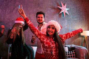 Portrait of a young woman with a glass of champagne at home on the foreground. Beautiful brunette in a Santa hat, red costume with deers photo