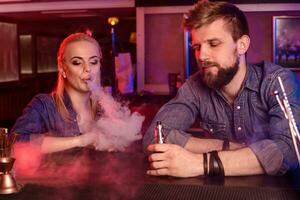 A man and woman smoking electronic cigarette in a vape bar. photo