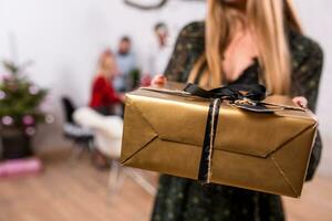 Focus on a giftbox in woman hands in the foreground. Beautiful blonde in a Santa hat and black dress photo