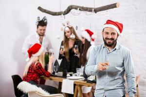 Shot of happy friends enjoying holidays. Focus on the man in the foreground in a red Christmas hat photo