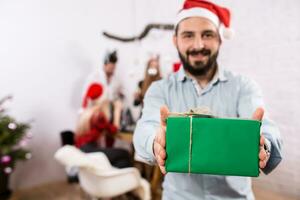 Shot of happy friends enjoying holidays. Focus on the man in the foreground in a red Christmas hat photo