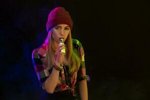 Vaping girl. Young hipster woman vape e-cig on black background. Hip-hop style. Studio shot photo