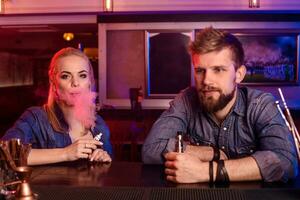 A man and woman smoking electronic cigarette in a vape bar. photo