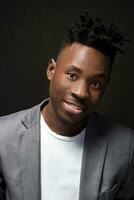 Close-up portrait of handsome black man with charming smile. Studio shot of well-dressed african guy wears white T-shirt and gray jacket. photo