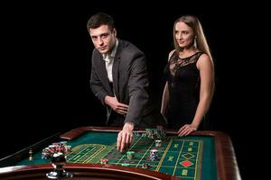 Elegant couple at the casino betting on the roulette, on a black background photo