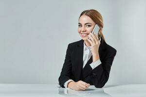 attractive dark-haired woman dressed in a black suit is sitting at  table in an office. photo