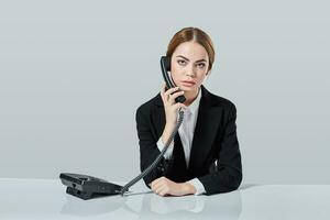 attractive dark-haired woman dressed in a black suit is sitting at  table in an office. photo