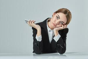 attractive dark-haired woman dressed in a black suit is sitting at  table in an office. photo