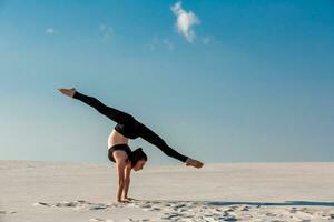 Young woman practicing handstand on beach with white sand and bright blue sky photo