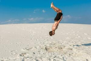 Portrait of young parkour man doing flip or somersault on the sand. photo