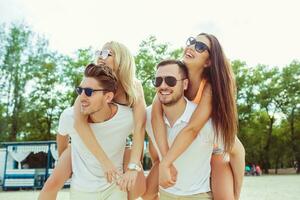 Group of friends walking along the beach, with men giving piggyback ride to girlfriends. photo