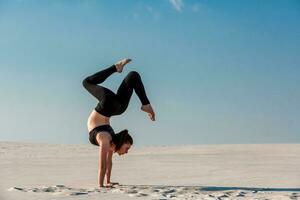 Young woman practicing handstand on beach with white sand and bright blue sky photo