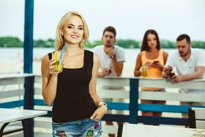 Blond girl on a summer terrace in a bar drinks cocktail photo