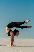 Young woman practicing handstand on beach with white sand and bright blue sky photo