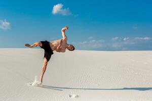 Portrait of young parkour man doing flip or somersault on the sand. photo