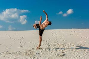 Portrait of young parkour man doing flip or somersault on the sand. photo