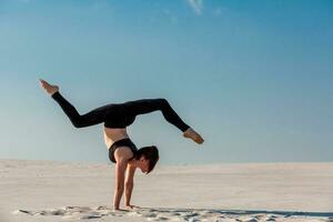 Young woman practicing handstand on beach with white sand and bright blue sky photo