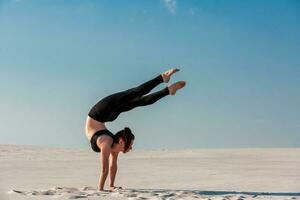 Young woman practicing handstand on beach with white sand and bright blue sky photo