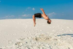 joven hombre saltando en el playa con blanco arena y brillante azul cielo foto