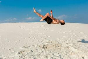 Portrait of young parkour man doing flip or somersault on the sand. photo