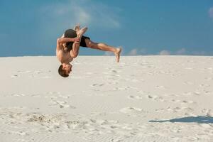 Portrait of young parkour man doing flip or somersault on the sand. photo